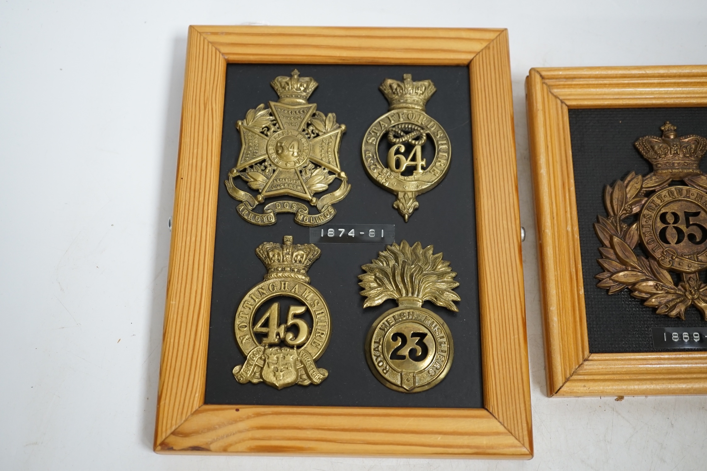 Five military helmet and shako plates mounted on two boards, including; the Nottinghamshire Regiment, the 2nd Staffordshire Regiment, the Royal Welsh Fusiliers, the Cumberland Regiment and the 85th King’s Light Infantry.